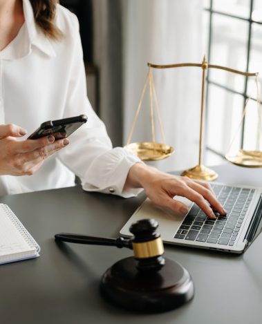 Conseil Juridique : Avocate connectée et outils de justice moderne Une avocate ou professionnelle du droit utilise son smartphone et un ordinateur portable, avec un maillet de juge et une balance de la justice en arrière-plan, symbolisant le droit numérique et la consultation juridique en ligne.